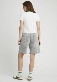 T-shirt blanc à manches courtes avec un col vert, associé à un short en jean gris avec deux poches arrière et une coupe décontractée. Baskets blanches avec des accents verts.