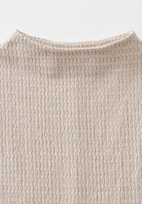 Gros plan sur un tissu beige tricoté avec un motif texturé en nid d'abeille et un détail d'encolure arrondie.