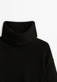 Pull en grosse maille côtelée noir à col roulé épais et replié sur fond blanc uni.