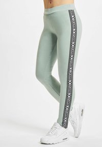 Mintgrønne leggings med høj talje, der har sorte sidelister med logo accenter. Parret med hvide atletiske sko.