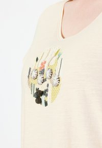 Crème korte mouwen shirt met decoratieve borduursels van verschillende texturen, waaronder ronde versieringen en kleurrijke draadpatronen.