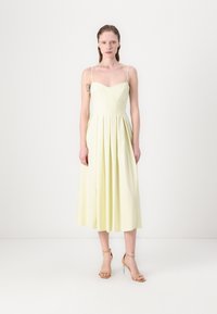 Rochie midi plisată de un galben deschis, cu decolteu în formă de inimă și bretele subțiri, confecționată dintr-un material ușor. Purtată cu pantofi cu toc nude.