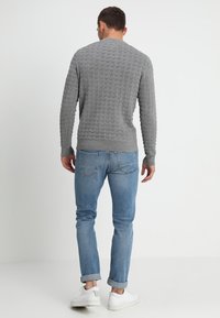 Maglione grigio con texture e orlo a coste, abbinato a jeans azzurri e sneaker bianche, visto da dietro.