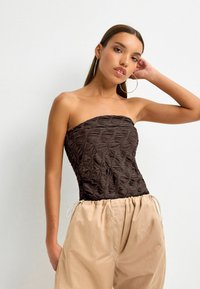 Brun strapless topp med texturerat bladmönster, kompletterad med beige dra åt byxor med lös passform och lätt material.