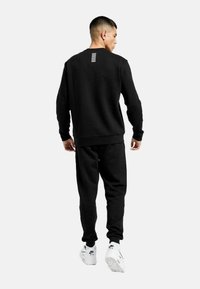 Felpa nera e pantaloni in tessuto morbido, con dettagli a striscia orizzontale sul retro; abbinati a scarpe da ginnastica bianche.