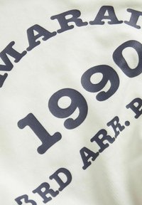 Tessuto bianco con testi stampati in blu scuro che recitano "NARAI 1990 3RD ARR. P." in grassetto, font serif arrotondato, disposti in linee curve.