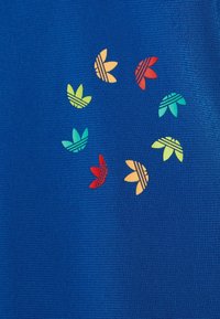 Circle of multicolored Adidas trefoil logos on a textured blue fabric background.