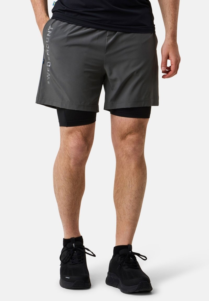 Grijze sportshorts met zwarte voeringen, voorzien van reflecterende logo-details aan de zijkant. Lichtgewicht en gladde textuur. Zwarte sneakers inbegrepen.