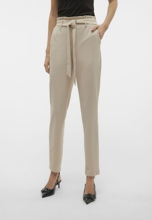 Pantaloni beige a vita alta con cintura a coulisse, tasche laterali e design a gamba affusolata, abbinati a décolleté nere a punta.