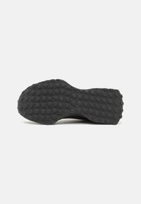 Semelle de chaussure noire avec un motif complexe de grips circulaires, texturée pour l'adhérence, présentant une forme courbée et en matériau en caoutchouc.