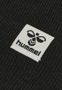 Svart stickat tyg med en vit etikett som har en logotyp och ordet "hummel" i svart text, sydd vid kanten.