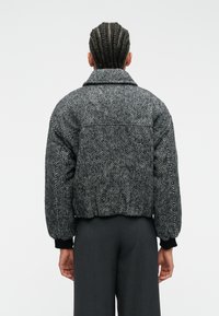 Veste courte à motif pied-de-poule noire et grise avec un large col, des manches bouffantes et des poignets côtelés noirs, portée sur un pantalon charbon.
