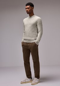 Ljusgrå stickad tröja med rundad halsringning, i kombination med bruna manchesterbyxor och beige sneakers med vita detaljer.