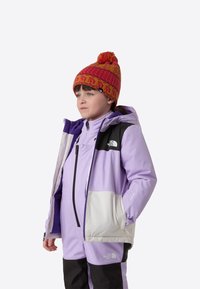 Lilla vanntett jakke med svart brystpanel, kombinert med en rosa strikket lue med dusk. Svart og lilla detaljer på dressen.