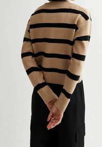 Pull beige et noir à rayures avec un ourlet et des poignets côtelés, doté d'une coupe décontractée et de manches longues. Mains visibles jointes derrière.