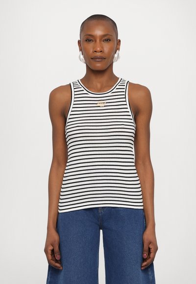 Débardeur sans manches noir et blanc rayé avec un col rond et une petite épingle dorée, associé à un pantalon en denim à jambes larges.