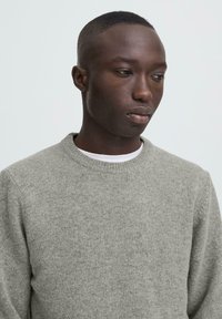 Grå stickad tröja med rund halsringning, med en mjuk textur och en avslappnad passform. Bärs över en vit skjorta, minimalistisk design.