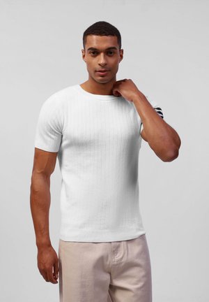 Witte gebreide trui met korte mouwen, ribbelstructuur, ronde hals en een contrasterende gestreepte accenten op de linker schouder.