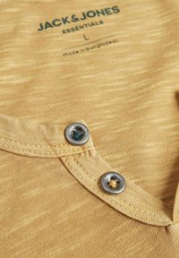 Camisa polo de algodón amarilla con un patrón texturizado, que presenta un cuello curvado y dos botones plateados con un acento de hilo azul.