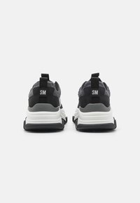 Černé a šedé sportovní boty s texturovanou síťovinou a semišovým svrškem, vybavené bílou mezipodešví a značenými poutky na patě.