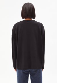 Schwarzer, übergroßer Langarm-Sweatshirt mit lockerer Passform, rundem Ausschnitt und breiten Bündchen, kombiniert mit blauen Jeans.