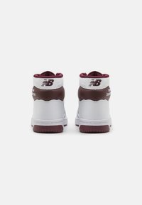 High-top sneakers made of white and maroon synthetic material, featuring a padded collar, textured accents, and a rubber sole.