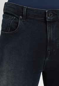 Dunkelblaue Jeans aus Denim mit klassischer Passform, ausgestattet mit einer Vordertasche und einem Metallknopfverschluss. Der Stoff hat eine glatte Textur mit leichter Ausbleichung.
