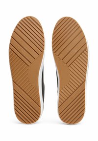 Weiße Sneaker mit einer strukturierten, braunen Gummisohle. Die Sohle verfügt über diagonale und horizontale Rillen für besseren Halt.