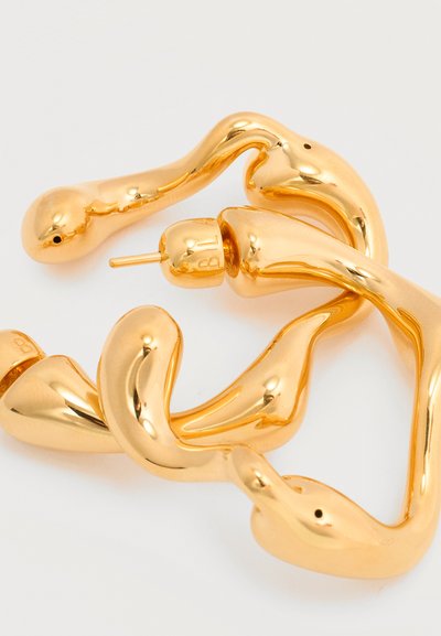 Στριμμένα, λαμπερά χρυσά μεταλλικά σκουλαρίκια-κρίκοι με ομαλή, ακανόνιστη οργανική μορφή και πίσω στερεώματα με καρφί, σε λευκό φόντο.