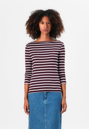Striped long-sleeve top in burgundy and white, featuring a wide neckline and a small logo detail, paired with a blue denim skirt.