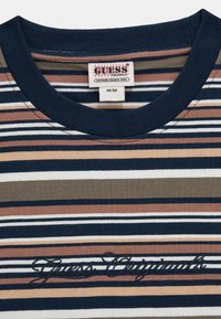 T-shirt en coton rayé comprenant des couleurs marine, pêche, blanche et olive. Il a un col ras du cou et "Guess Originals" brodé en noir.