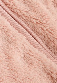 Tissu rose duveteux avec une surface douce et texturée, présentant une bande élastique rose lisse contrastante le long du bord.