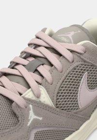 Κοντινός πλάνους ενός γκρι και ροζ παπουτσιού Air Jordan που δείχνει τις κορδόνες, το πλέγμα στη πλαϊνή πάνελ, το σήμα Nike και το λογότυπο Jumpman υλικό από σουέτ.