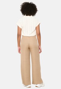 Cream knitted short-sleeve top with a loose fit, paired with light brown wide-leg striped pants and white sneakers.