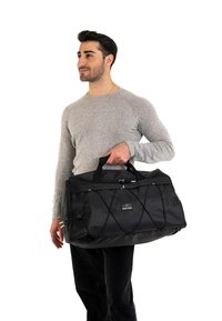 Black duffel bag with textured fabric, handles, and elastic cord detail. The bag features a logo and a zip closure at the top.