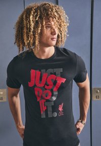 Svart t-skjorte med fet rød og grå "JUST DO IT." grafikk, med Liverpool FC-logo. Korte ermer og rund hals.