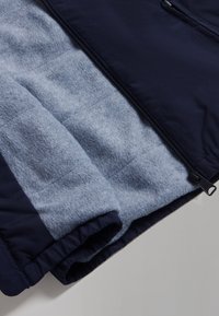 Marinblå polyesterväst med ett mjukt grått fleecefoder; har en smidig dragkedja och kviltad textur på insidan.