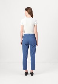 Blue cotton trousers with a straight-leg design, featuring a back pocket and a smooth texture. Worn with a fitted white short-sleeve top.