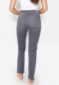 Grijze denim jeans met een aansluitend ontwerp, rechte pijpen, subtiele stikdetails en twee achterzakken. Draagbaar op blote voeten, waarbij de enkels zichtbaar zijn.