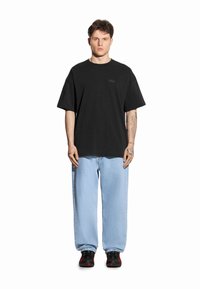 Czarna koszulka z krótkim rękawem z subtelnym logo, zestawiona z jasnoniebieskimi luźnymi dżinsami i czarnymi trampkami z czerwonymi akcentami.