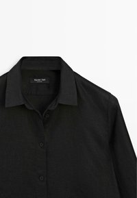 Zwart overhemd met knoopsluiting en klassieke kraag, plat uitgestald, met bovenkant vooraan en merklabel "Massimo Dutti" zichtbaar.