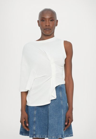 Top bianco a maniche corte con dettagli in tessuto drappeggiato e orlo asimmetrico, abbinato a una gonna di denim. Texture liscia; design minimalista.