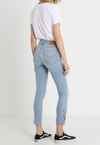 Jeans de tiro alto en azul claro con un ajuste ceñido, fabricados en material de mezclilla, con detalles de lazo en el tobillo y un parche de cuero en la parte posterior.