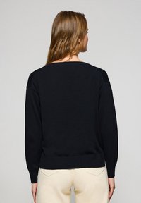 Schwarzer Pullover mit lockerer Passform, langen Ärmeln und geripptem Saum. Weiches Baumwollmaterial mit kontrastierenden Schulterakzenten. Einfaches, einfarbiges Design.