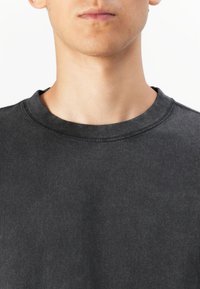 Tricou din bumbac de culoare gri închis, cu decolteu rotund, textură subtilă și cusături contrastante pe guler și șinele umerilor.