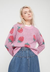 Ροζ πλεκτό πουλόβερ με σχέδιο φράουλας σε κόκκινες και πράσινες αποχρώσεις, σε συνδυασμό με μπλε τζιν φούστα. Μαλακή υφή και άνετη εφαρμογή.