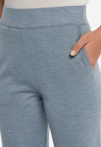 Ljust blå stickade byxor med bred midjeband, ficka på höger sida och mjukt, texturerat tyg med subtila sömnadsdetaljer.