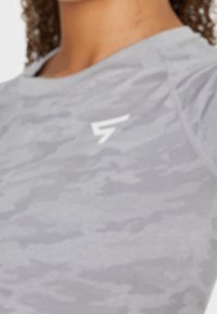 Grau camoufliertes Sportoberteil mit Rundhalsausschnitt. Verfügt über ein weißes Logo auf der Brust und strukturierter Stoff.