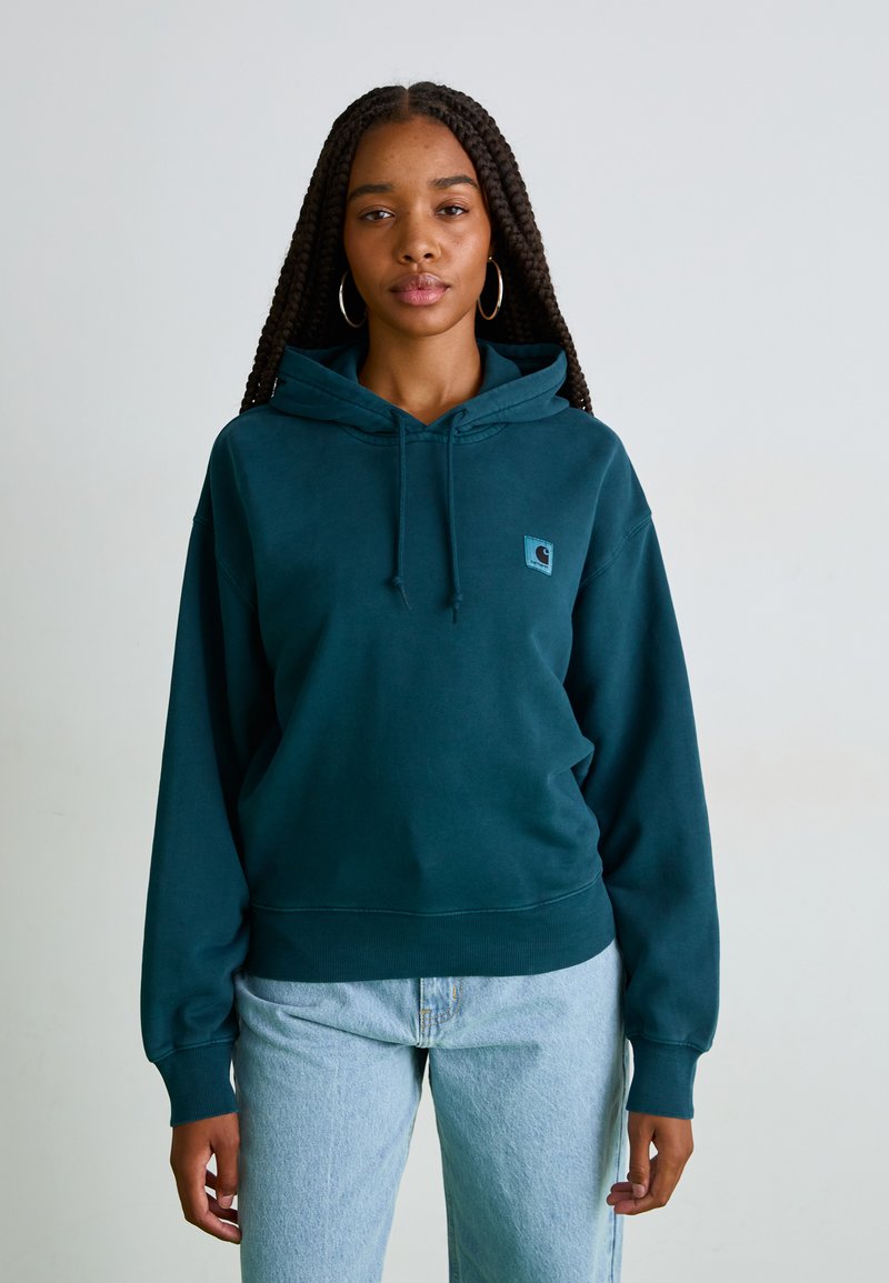 Sweatshirt à capuche bleu-vert en tissu doux, avec une poche avant et des poignets côtes, arborant un petit patch logo sur la poitrine.