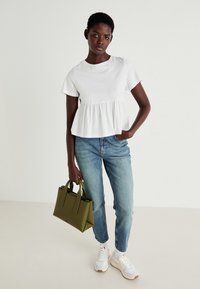 Top peplum blanc à manches courtes avec col rond, associé à un jean droit bleu clair. Accessoirisé avec un petit sac à main vert olive.